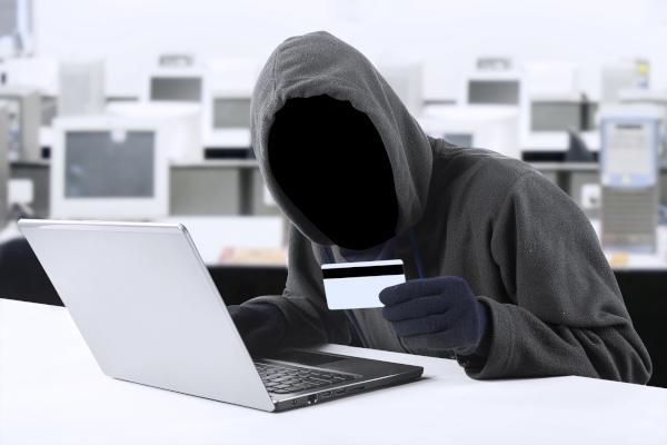 Internet Theft - a man wearing a balaclava and holding a credit card while sat behind a laptop